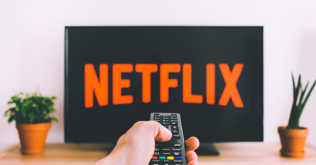 A hand holding a TV remote in front of a screen with a streaming app, perfect for streaming and movie night themes.